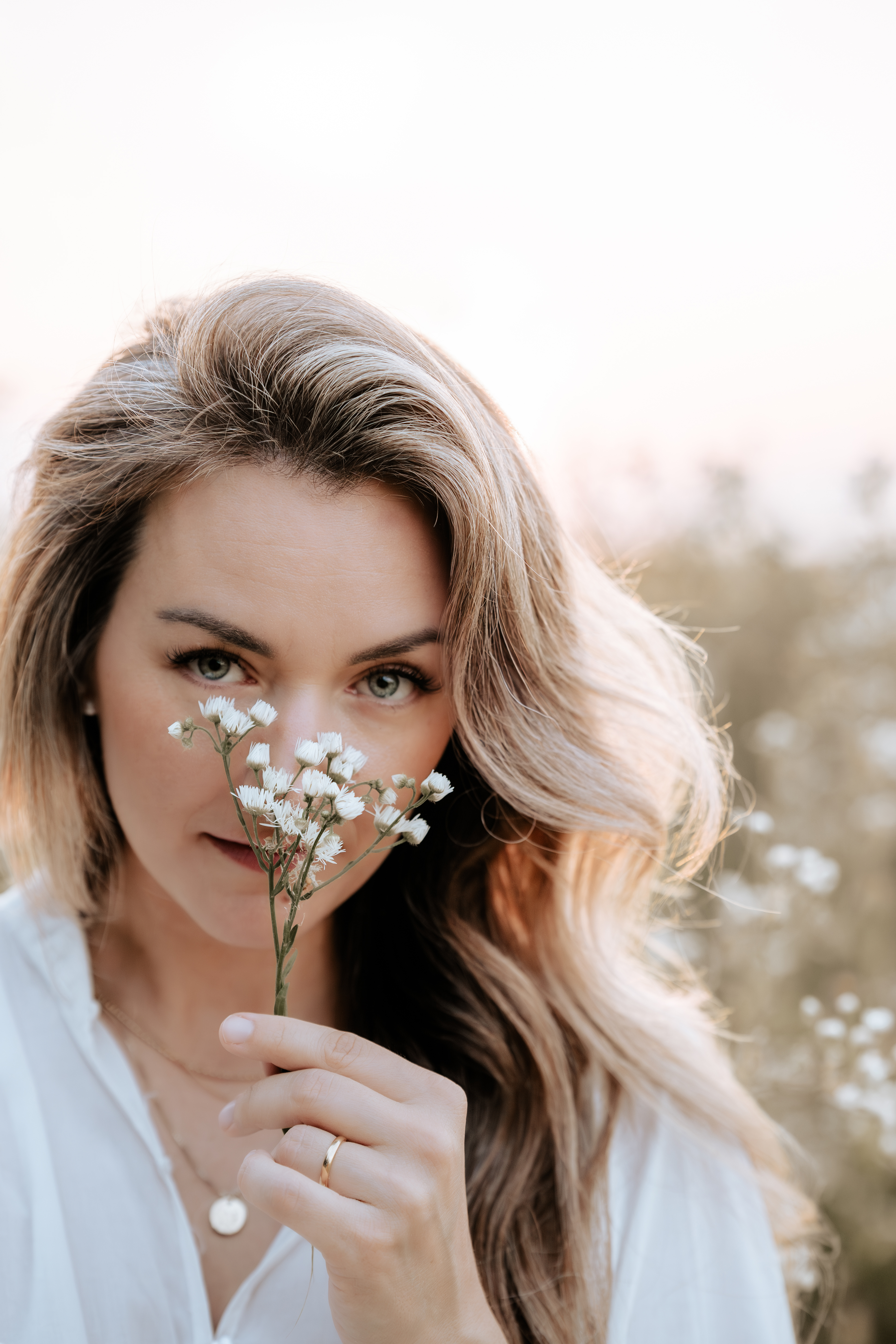 Stephanie Bertani im Gegenlicht, eine Wiesenblume vor dem Gesicht